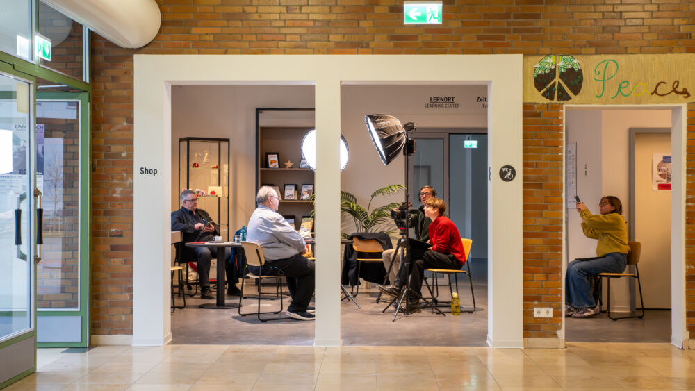 Im Zeitzeugeninterview berichtet der ehemalige Pfarrer im Notaufnahmelager Gießen, Matthias Leschhorn, der GEDG-Mitarbeiterin Margarete Puhl (GEDG) und Johannes Romeyke (musealis) von seinen Erfahrungen. Dahinter dokumentiert Leona Ludwig (GEDG) für die Öffentlichkeitsarbeit, 5. Dezember 2025 (Christian Faludi/GEDG)